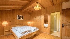 Une pièce en bois avec un lit, une porte donnant accès à une douche et un tableau encadré au mur.