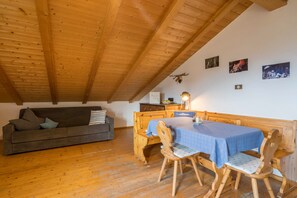 Un plafond en bois, un canapé, une table avec des chaises et des tableaux accrochés au mur.