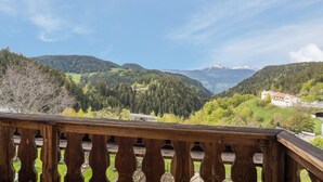 Une balustrade en bois surplombe un paysage montagneux, avec un bâtiment visible au loin.