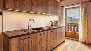 Une cuisine dotée de meubles en bois, d’un évier en acier inoxydable et d’une fenêtre donnant sur un paysage boisé.