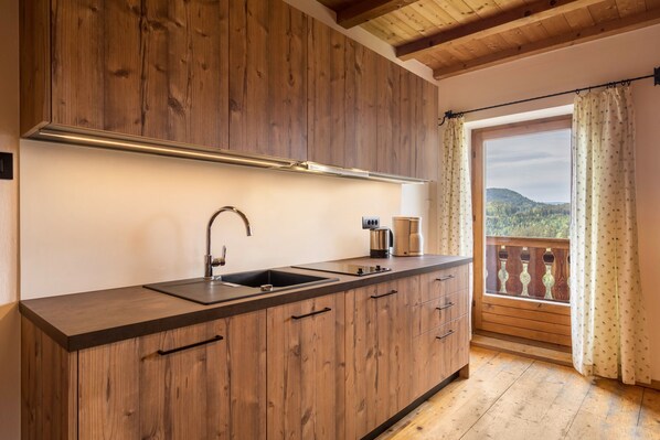 A kitchen with wooden cabinets, a stainless steel sink, and a window with a view of a forested landscape.