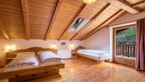 Une pièce au plancher de bois, dotée de deux lits, d’une lucarne et d’une fenêtre donnant sur un paysage verdoyant.