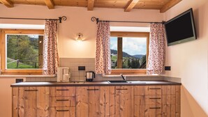 Une cuisine avec des meubles de rangement en bois, une machine à café, une bouilloire et un téléviseur fixé au mur.