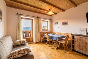 A cozy room with a wooden ceiling, a dining table with chairs, a sofa, and a view of mountains through the windows. - Apartment "Sonnenblume - Nusserhof" near Skiing Area with Mountain Views & Balcony (Hafling)