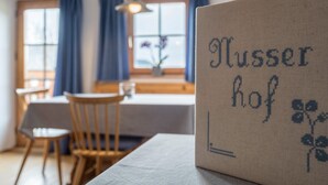Ein Zimmer mit Tisch, Stühlen, einem Fenster mit Vorhängen und einer Wand mit einem gerahmten Text.