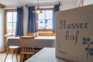 Une pièce comprenant une table, des chaises, une fenêtre avec des rideaux et un mur orné d’un texte encadré.