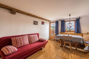 Une pièce chaleureuse avec un canapé rouge, une table à manger en bois et une fenêtre avec des rideaux.