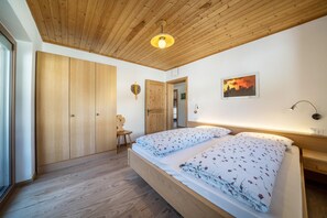 Un dormitorio con techo de madera, una cama con ropa de cama floral, una mesita de noche, una silla y una puerta que da a otra habitación.