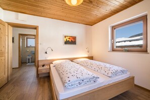 A bedroom with a wooden ceiling, a bed with floral bedding, a window with a snowy view, and a painting on the wall.