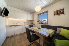 A modern kitchen with white cabinets, a wooden dining table, black chairs, a green table runner, and a black sofa with green cushions.