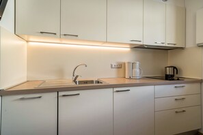 A modern kitchen with white cabinets, a stainless steel sink, a coffee maker, and a range hood.