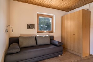 A modern living room with a dark sofa, a wooden wardrobe, a window with a view, and a wall-mounted light fixture.