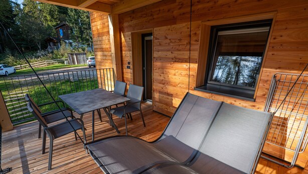 A wooden deck with a table and chairs, a reclining chair, and a window overlooking a forest. - Apartment "Hirzer" near Skiing Area with Forest View, Wi-Fi, Balcony & Shared Garden (Falzeben)