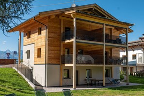 A two-story wooden building with balconies, a patio area, and a view of the mountains.