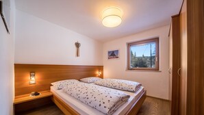 Makuuhuoneessa on puinen sängynpääty, kaksi sänkyä, yöpöytä, seinään kiinnitetty lamppu, ikkuna, josta on näkymä, ja ovi.