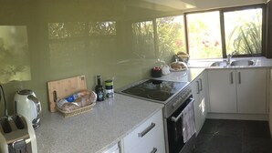 Une cuisine dotée d’un plan de travail en granit, d’un grille-pain, d’une bouilloire, d’une planche à découper, d’un panier de pain et d’une fenêtre donnant sur un paysage verdoyant.