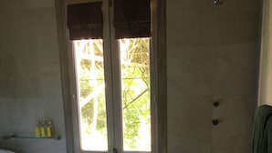 Une salle de bain dotée d’une baignoire sur pieds, d’un espace douche et d’une porte donnant sur un espace extérieur lumineux.