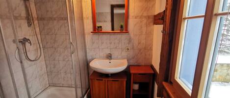 Un baño con ducha, lavamanos y un ventanal pequeño.