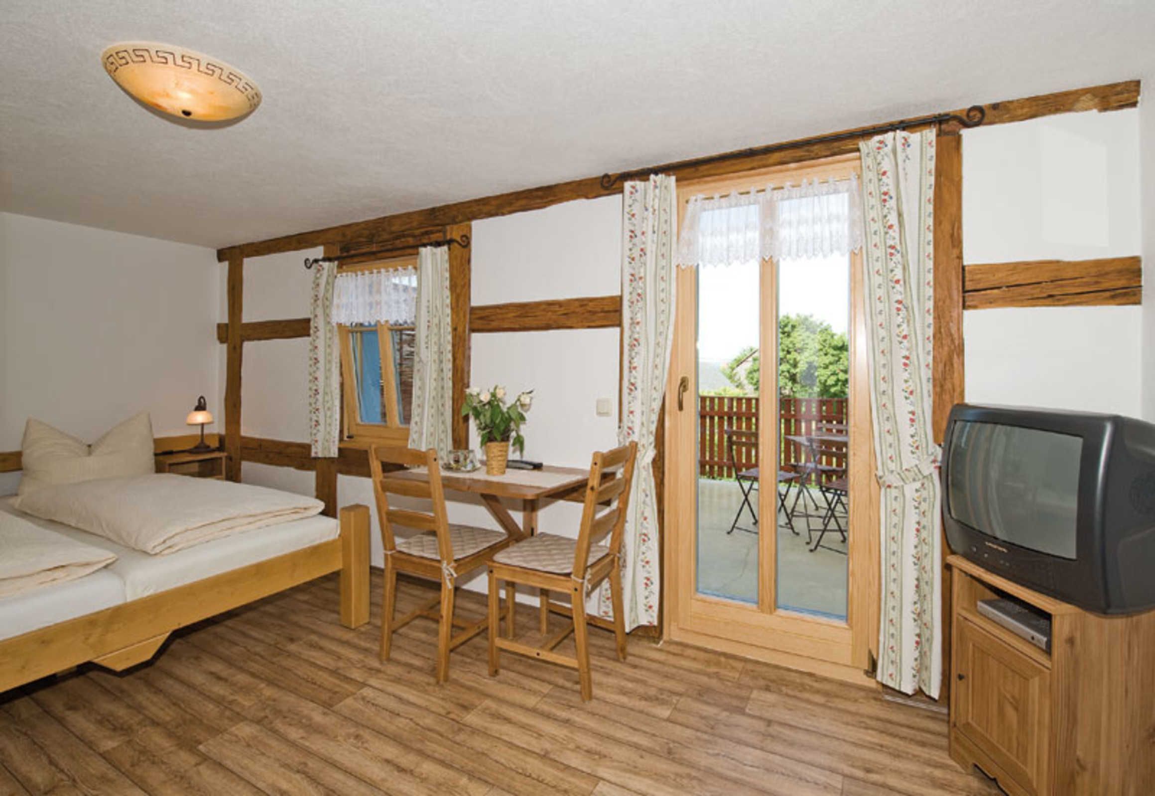 Een gezellige kamer met een bed, een eettafel met stoelen, een televisie en een schuifdeur naar een terras.