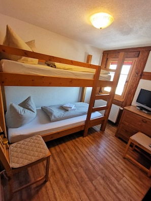 Una stanza con letto a castello, una scrivania, una sedia, pavimento in legno e una finestra con vista.