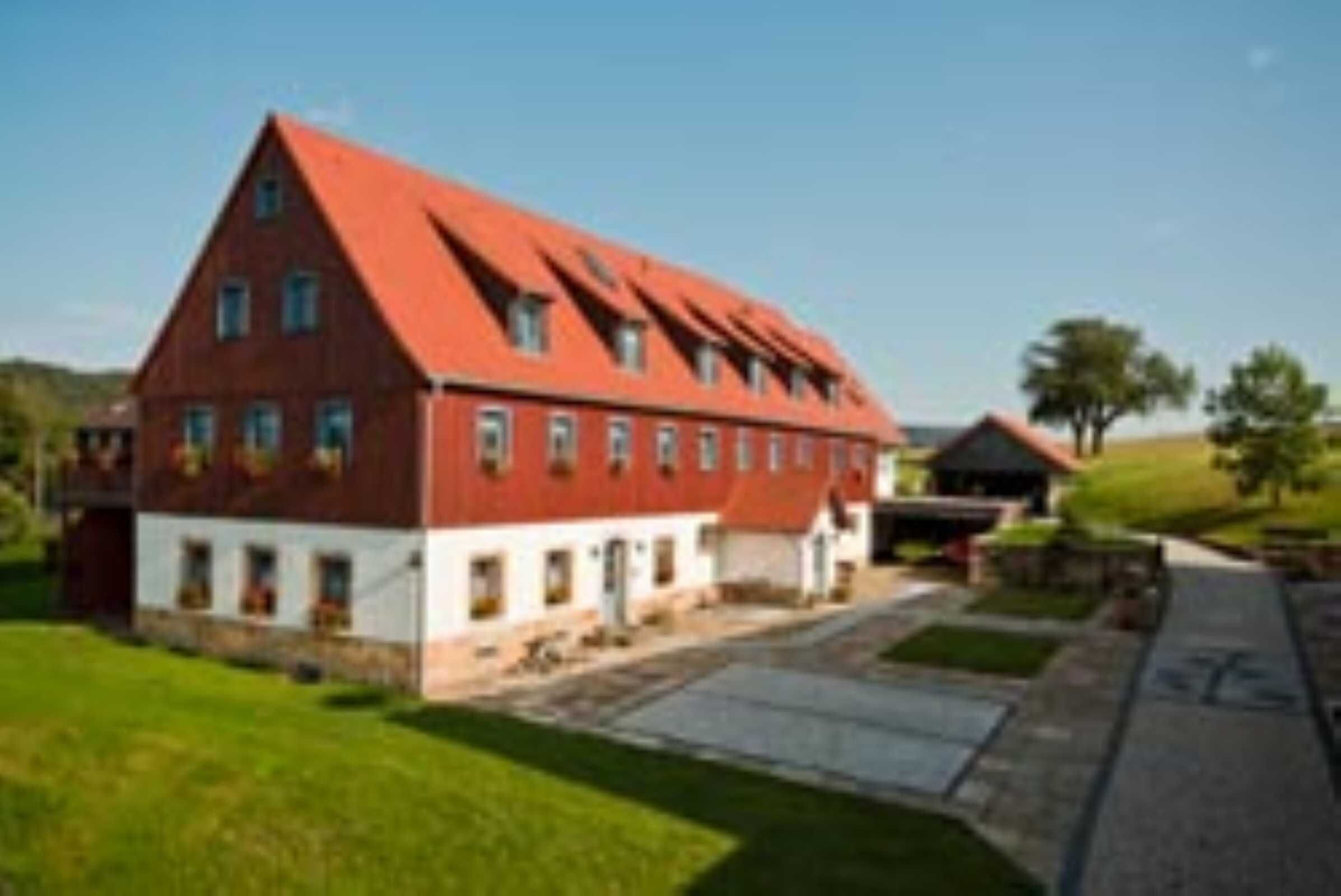 Ein großes Gebäude mit rotem Dach, mehreren Fenstern, einer gepflasterten Auffahrt und einer Rasenfläche.