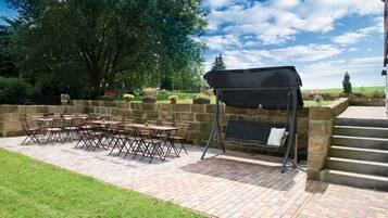Eine Terrasse im Freien mit Backsteinboden, Grill und Tisch mit Stühlen.