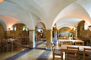 An interior with stone arches, wooden tables, and chairs arranged for dining. - Ferienwohnung Kornkammer - Pension Bauernhaus Vetter (Gohrisch)