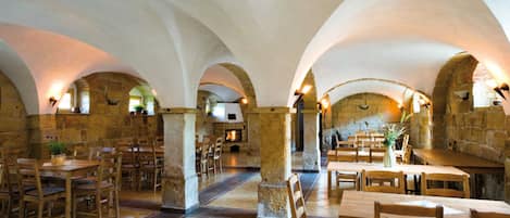 An interior with stone arches, wooden tables, and chairs arranged for dining.
