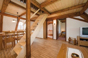 A spacious loft with exposed wooden beams, a wooden staircase, a dining area with wooden chairs, a television, and a cozy seating area.