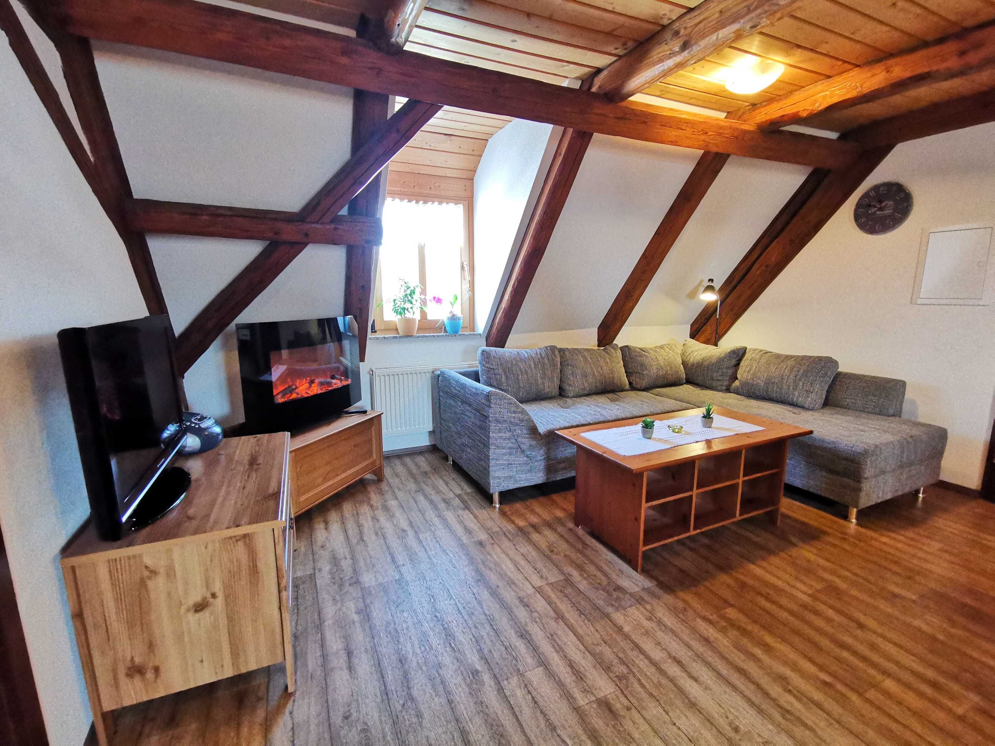 Een gezellig zolderkamer met zichtbare houten balken, een open haard, een bank en een televisie.
