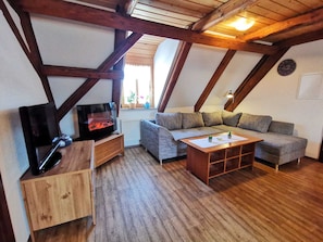 A cozy attic room with exposed wooden beams, a fireplace, a sofa, and a television.