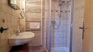 Une salle de bain équipée d’un lavabo, d’un miroir, d’un porte-serviettes, d’une douche et d’un sol carrelé.