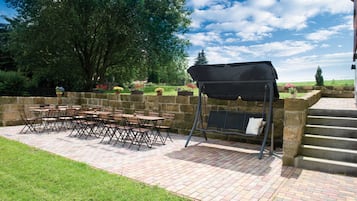 Eine Terrasse im Freien mit Backsteinboden, Grill und Tisch mit Stühlen.