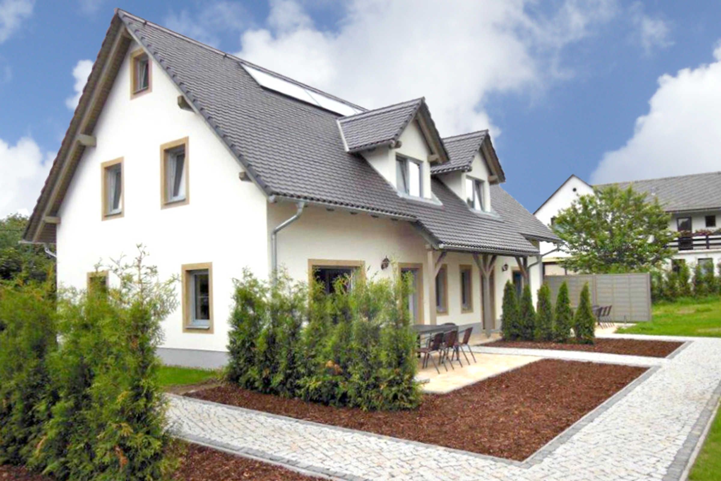 Ein zweistöckiges Haus mit geneigtem Dach, einer Veranda und einem angelegten Garten mit einem Weg.
