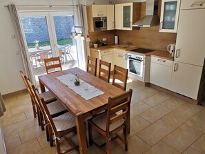 Une cuisine moderne avec des meubles blancs, un four encastré et un coin repas comprenant des chaises et une table en bois.