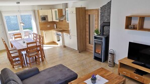 Una sala de estar moderna con un sofá, una mesa de centro de madera y un televisor. Cuenta con una zona de cocina con armarios y una estufa.