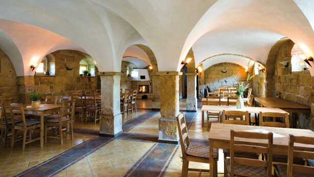 Un interior con arcos de piedra, mesas y sillas de madera dispuestas para comer.