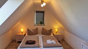 Un dormitorio en ático acogedor y bien iluminado, con una cama grande, dos mesitas de noche con lámparas y una ventana con persianas.