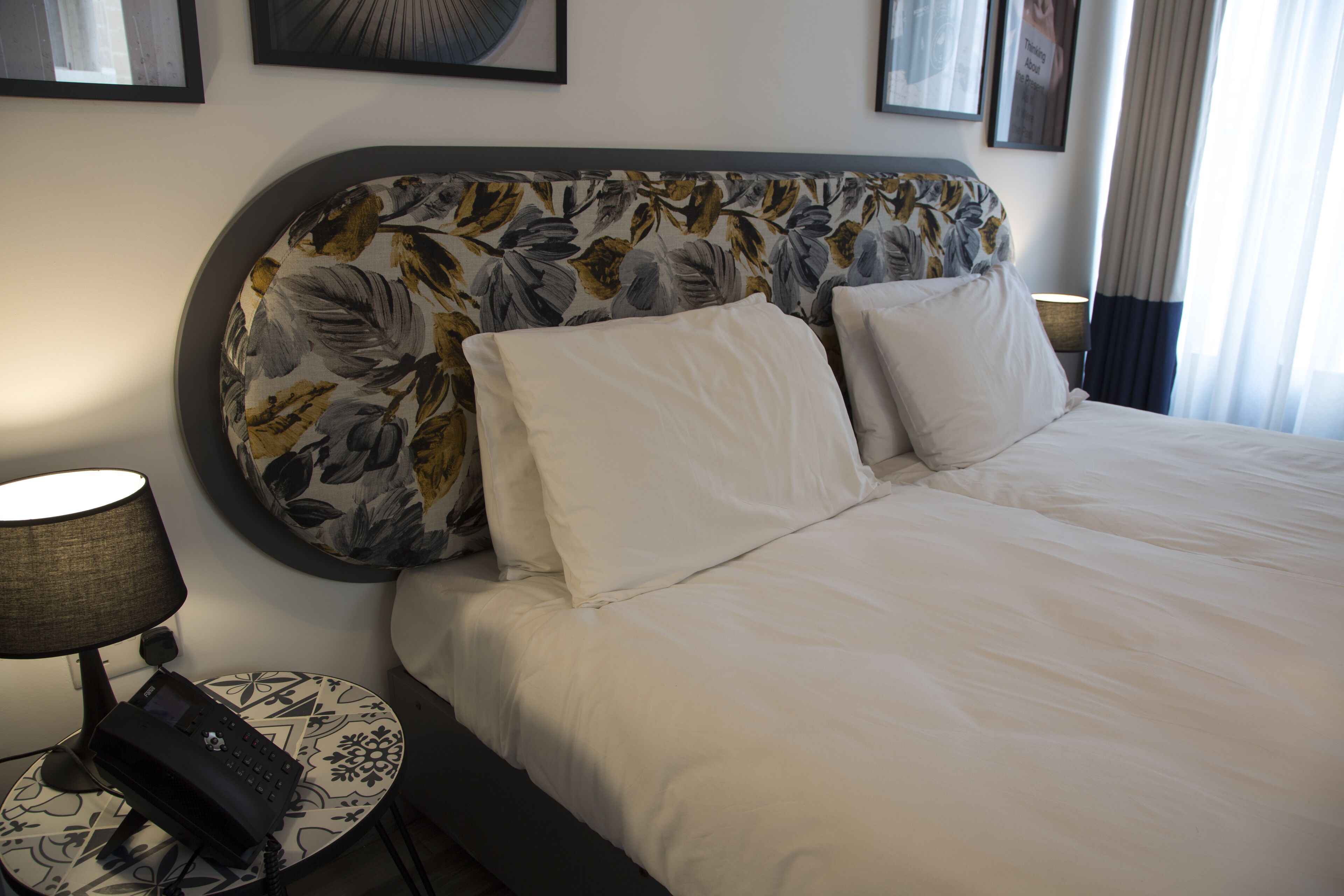 Una habitación de hotel con una cama grande, una mesita de noche con una lámpara y un teléfono.