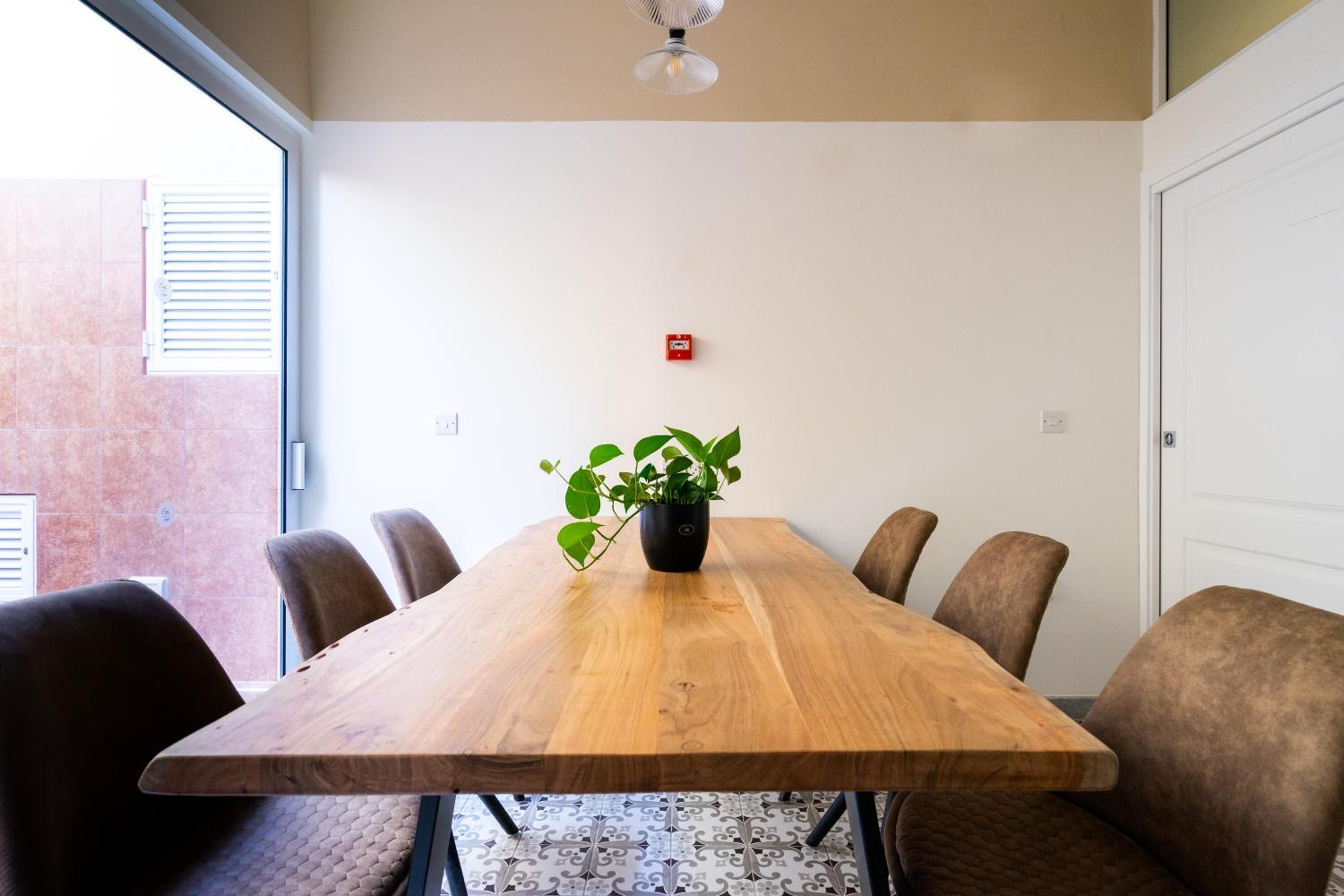 Uma sala de conferência com uma mesa de madeira, seis cadeiras, uma planta em vaso e um ventilador de teto.