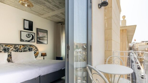 A bedroom with a bed, a nightstand, and a balcony with a table and chairs. - Lady Todd (Sliema)