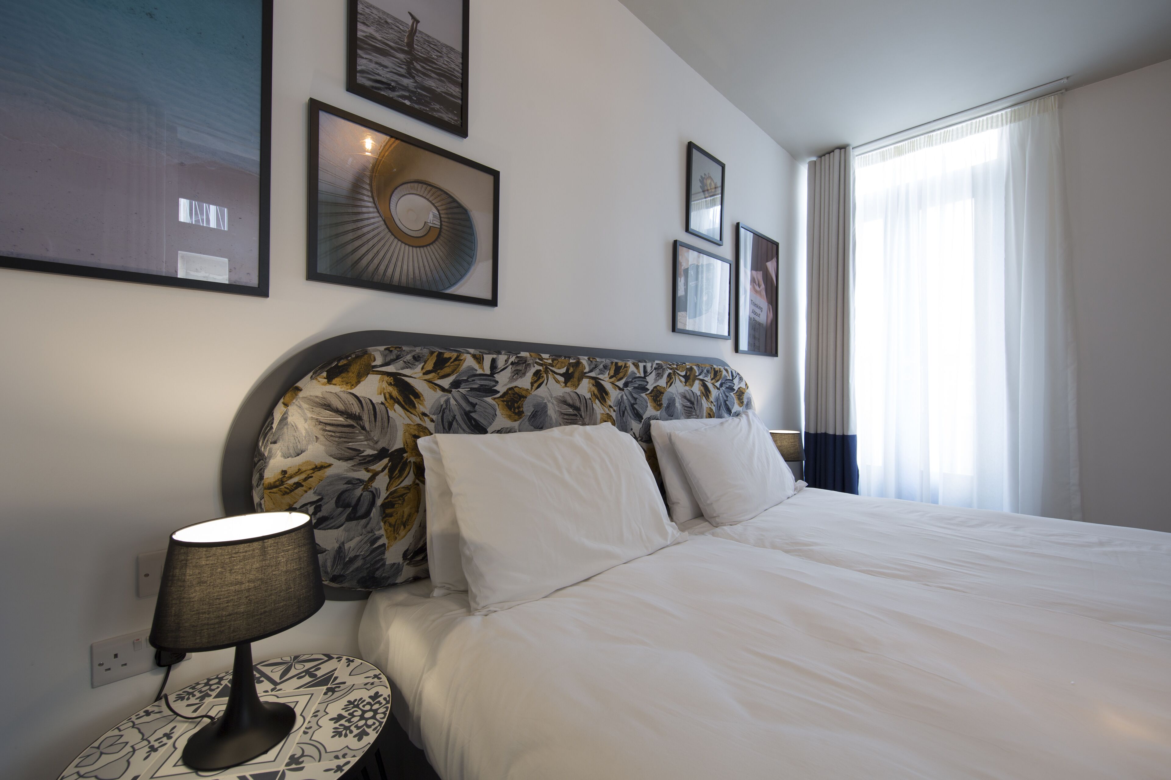 A hotel room with a large bed, a nightstand with a lamp, and several framed pictures on the wall.