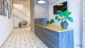 A reception area with a counter, a potted plant, a chair, and a staircase in the background. - Lady Todd (Sliema)