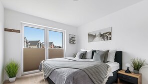 A bedroom with a bed, a nightstand, a potted plant, and a window with a view of houses. - Fine - two bedrooms, covered terrace, parking (Büsum)