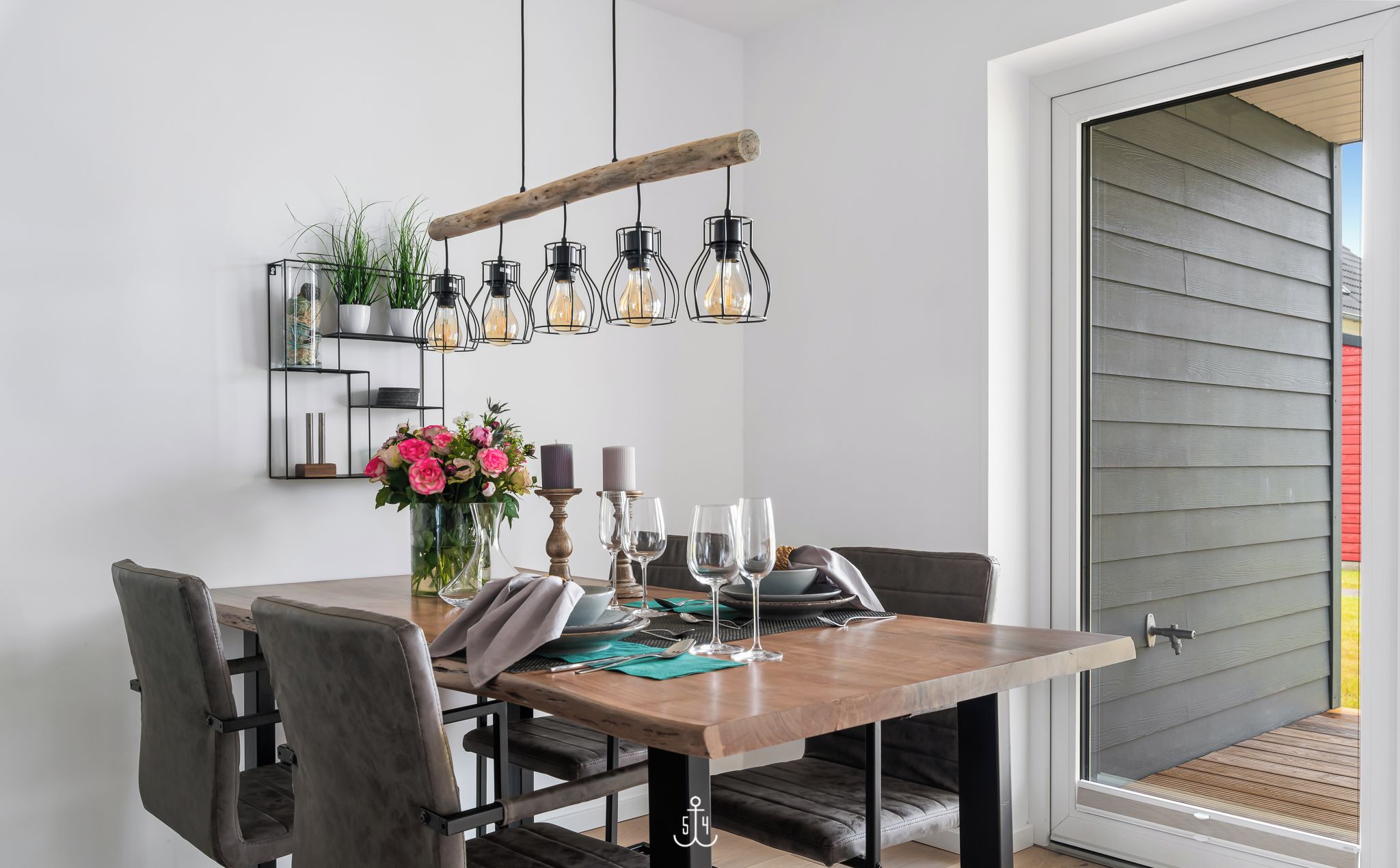 A dining area with a wooden table, four chairs, a vase with flowers, and hanging light fixtures.