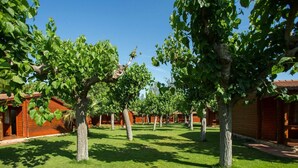 A row of wooden cabins with a well-maintained lawn and trees in the foreground. - Beachside Bungalow Escape (Cambrils)