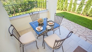 Uma varanda com uma mesa posta para dois, cadeiras e vista de um jardim bem cuidado.