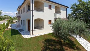 A two-story house with a white exterior, multiple balconies, and a stone pathway leading to the entrance. - Apartment with pool, 3 persons, garden, air-conditioned, family-friendly (Nova Vas)