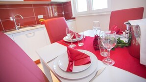 A dining area with red chairs and a table set for two, including plates, glasses, and a silver pitcher. - Apartment with pool, 3 persons, garden, air-conditioned, family-friendly (Nova Vas)