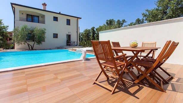 A poolside area with wooden chairs and a table, a swimming pool, and a building with balconies. - Apartment with pool, 3 persons, garden, air-conditioned, family-friendly (Nova Vas)